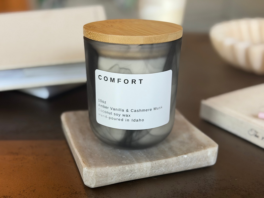 Black jar Comfort candle with wood lid, Amber Vanilla & Cashmere Musk scent, on travertine stand