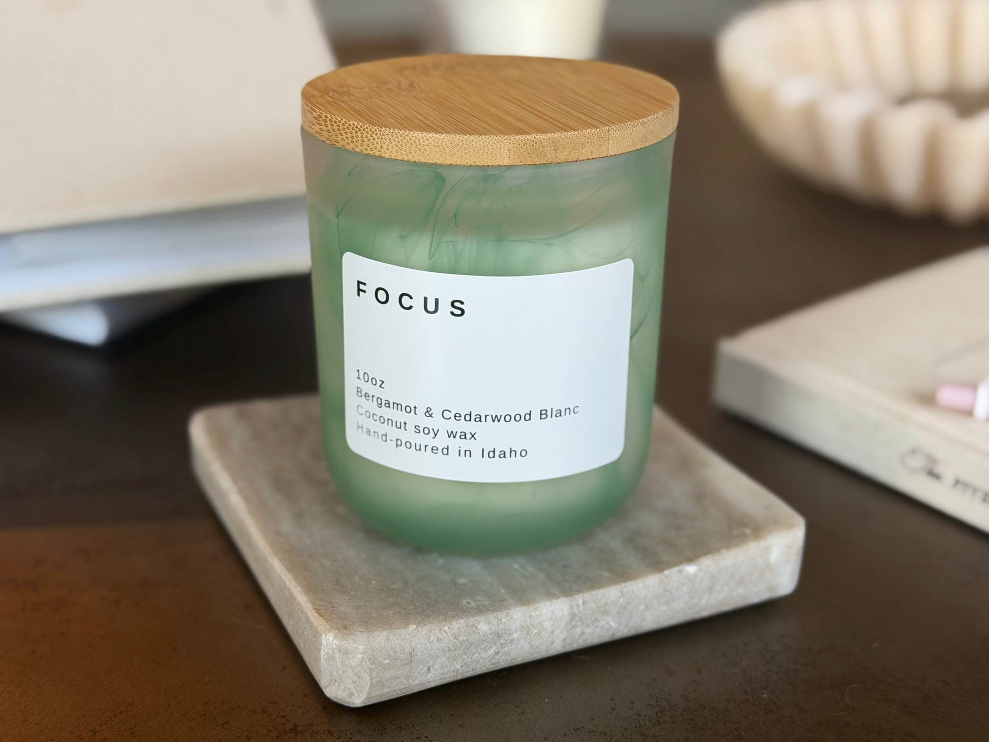 Frosted sage green Focus candle with wood lid, Bergamot &  Cedarwood Blanc scent, on travertine stand