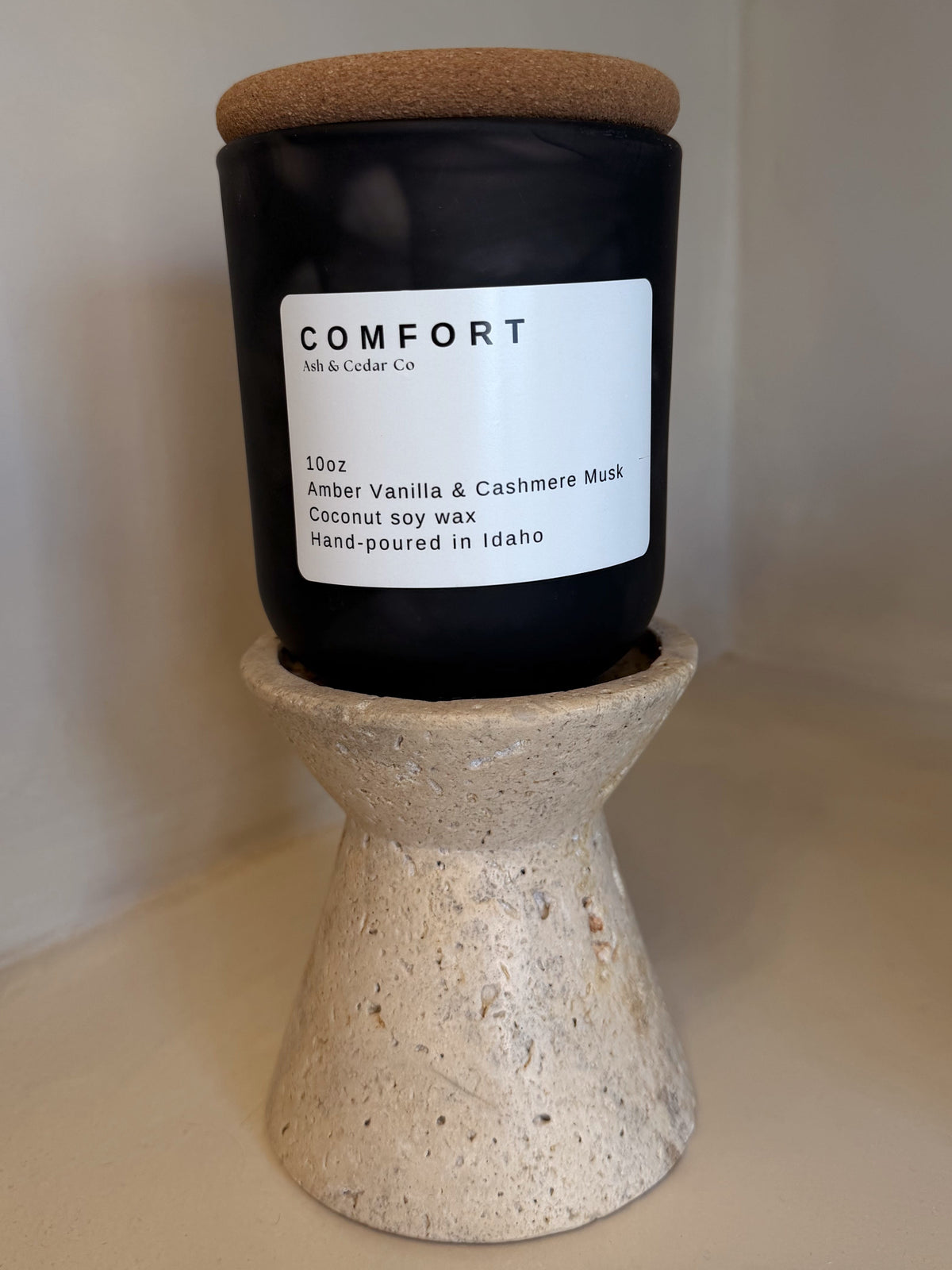 Black jar Comfort candle with cork lid, Amber Vanilla & Cashmere Musk scent, on travertine stand